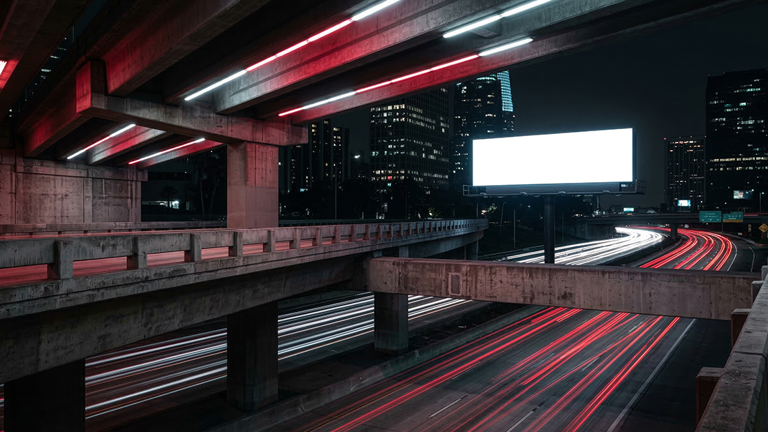 Long exposure night traffic light trails blurred beneath a blank billboard template on a cinematic urban highway.